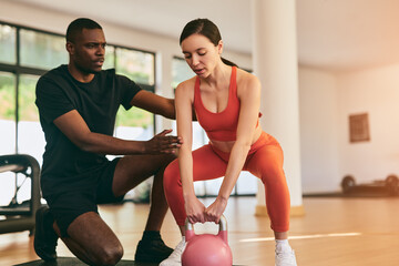Trainer helping woman doing exercise with kettlebell at gym
