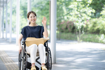 車椅子に乗る若い女性　手を振って挨拶