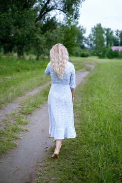 Portrait of blonde woman in a park. Young woman in blue vintage dress. Female walks in summer nature barefoot . Long hair.
