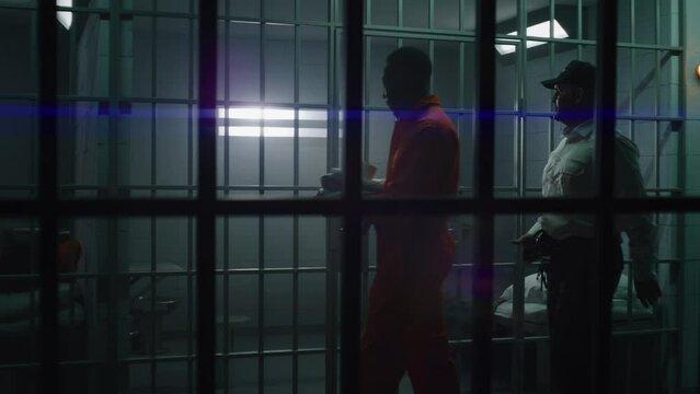 Warden brings new prisoner in jail cell and takes off his handcuffs. African American criminals serve imprisonment term in correctional facility or detention center. Guilty murderers in prison cells.