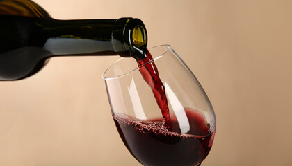 Pouring red wine into glass from bottle against blurred beige background, closeup. Space for text