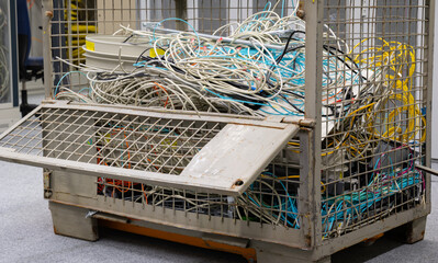 Im Rechenzentrum sind alte Netzwerkkabel und Stromkabel in einer Gitterbox zur Entsorgung gelagert - 630964047