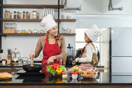 Happy moment asian mother and daughter cooking breakfast salad in the kitchen. Mom and daughter asian family having fun preparing healthy food vegetable. Positive parent and kid nice relationship