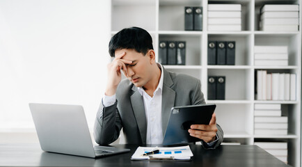 Fototapeta premium Frustrated young businessman working on a laptop computer sitting at his working place in office