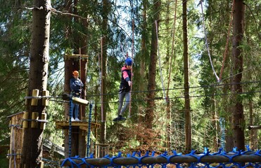 Man and a woman climb the wooden stairs at a height in amusement rope park