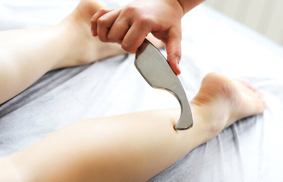 Instrumental mobilization of soft tissues by blades. Therapist using IASTM device treatment, girl for the treatment of soft tissues on the leg with guasha stainless steel instrument, osteopathy