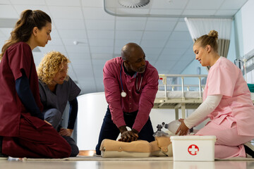 Senior african american male doctor with diverse trainee doctors learning cpr on model at hospital