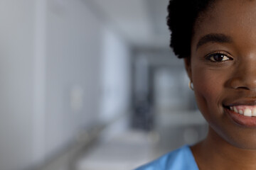 Portrait of happy african american female doctor wearing scrubs in corridor at hospital, copy space