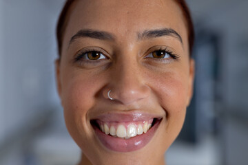 Portrait of happy biracial female doctor with nose piercing in corridor at hospital - obrazy, fototapety, plakaty