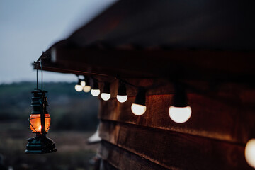 Storm lantern and festoon lighting by a cosy wooden cabin, Wales