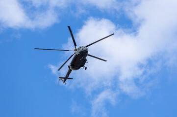 Silhouette of a helicopter flying in the blue sky with clouds