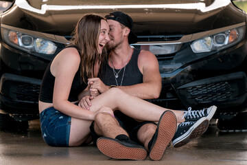 A guy and a girl sitting in front of the car at the carwash