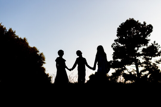 Silhouette of children holding hands in front of trees