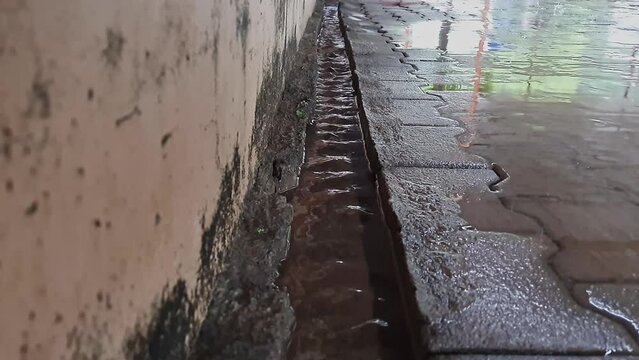 A view of rainwater cascading through a small ditch at the side of a building wall