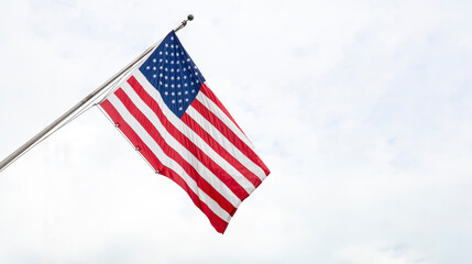 United States of America flag on a pole waving on cloudy sky background.