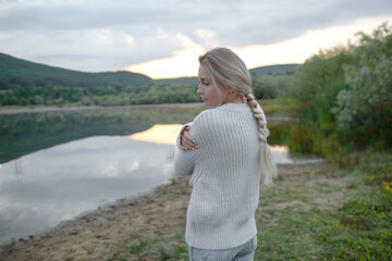 Back view of the blond woman dressed sweater and jeans., Walking in the shore of the lake with beautiful landskape. The girl enjoy the nature  in her trip