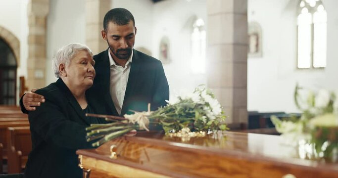 Funeral, church and elderly mother and man mourning death by coffin with flowers. Grief, family and son with mom by casket to comfort, support or interracial empathy for depressed or sad senior woman