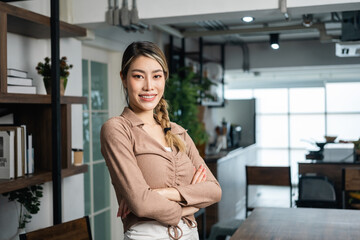 Fototapeta na wymiar Young asian business woman standing post near desk in home office. Beautiful business female in suit working at home holding pen. Attractive woman smiling looking at camera.