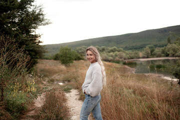Naklejka na ściany i meble the blond woman dressed sweater and jeans., Walking in the shore of the lake with beautiful landskape. The girl enjoy the nature in her trip