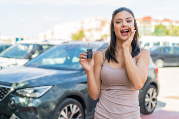 Young pretty woman holding car keys at outdoors shouting with mouth wide open