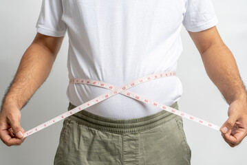 Man touching his fat belly on white background. Paunch of a man. Overweight tape measure around the waist