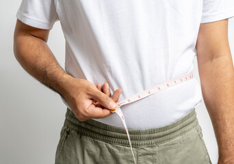 Man touching his fat belly on white background. Paunch of a man. Overweight tape measure around the...