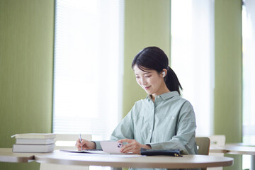 図書館にてスマートフォンを使用して勉強をする日本人の女性