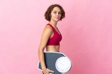 Young English woman isolated on pink background with weighing machine
