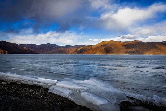 A winter scene unfolds at Pangong Lake, Ladakh, as ice plates stack up along the serene shoreline, offering a mesmerizing sight under the soft glow of the blue hour