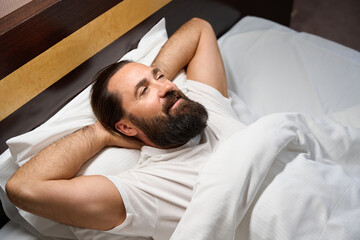 Middle-aged man lies on a snow-white bed