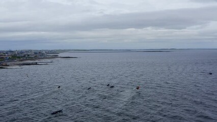 Aerial parallax around currach boat paddling out towards open ocean on grey sky day