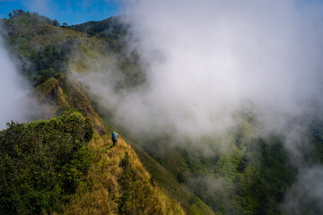 Fototapeta na wymiar a person with blue backpack and camera standing in the middle of mountain range and sea of cloud in northern of thailand (Nan province, Thailand) เด่นช้างนอน