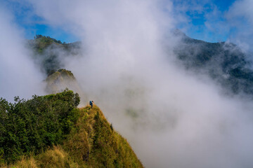 a person with blue backpack and camera standing in the middle of mountain range and sea of cloud in northern of thailand (Nan province, Thailand) เด่นช้างนอน