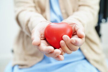 Asian elder senior woman patient holding red heart in hospital.