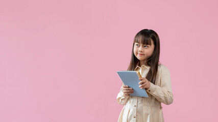 A cute young Asian girl is holding books and looking aside, an isolated pink background