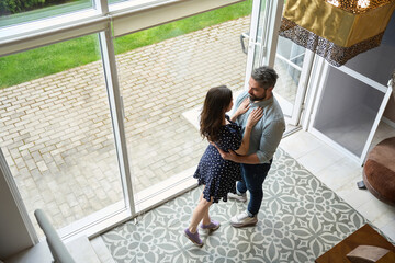 Happy husband and wife are standing embracing in spacious living room