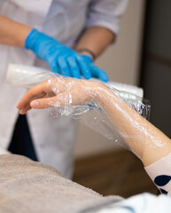 close-up masseur makes a hand massage in a beauty salon wrapping with film and cellophane
