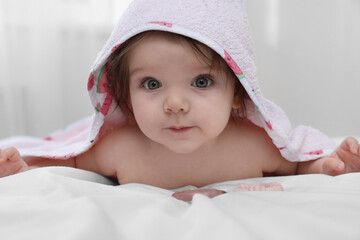Cute little baby in hooded towel after bathing on bed at home