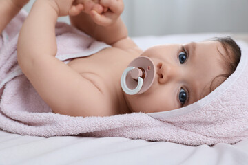Cute little baby with pacifier in hooded towel after bathing on bed, closeup