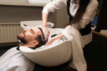 Handsome man enjoys procedure of washing his hair in barbershop