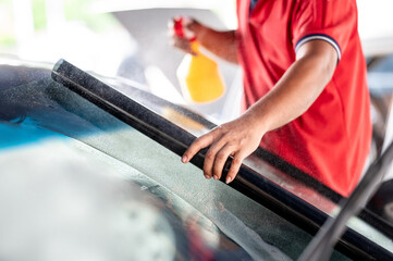 Male auto specialist worker hand spraying soapy solution while rolling car window film on front windscreen glass surface. Car side window film removal and tinting installation. 