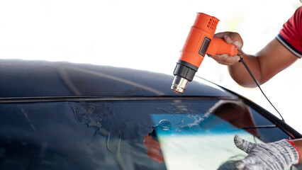 Auto specialist worker hand blowing hot air dryer or hairdryer removing old car window film tint...