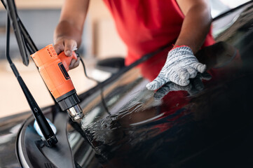 Auto specialist worker hand blowing hot air dryer or hairdryer removing old car window film tint...