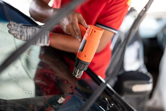 Auto specialist worker hand blowing hot air dryer or hairdryer removing old car window film tint and installing the new one. Car front windscreen film removal and tinting installation