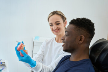 Fototapeta premium Dental technician showing dental prosthesis to African American client