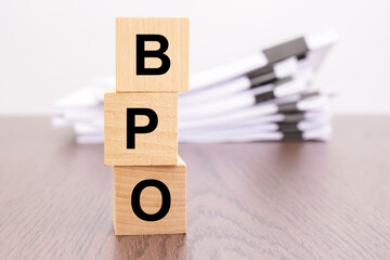 wooden cubes with letters BPO arranged in a vertical pyramid, stack white paper on background,...