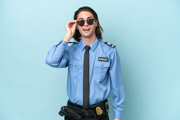 Young police caucasian man isolated on blue background with glasses and surprised