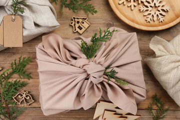 Furoshiki technique. Gift packed in fabric, thuja branches and festive decoration on wooden table, flat lay