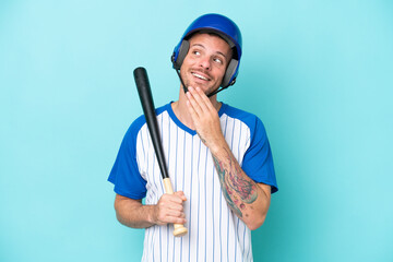 Baseball player with helmet and bat isolated on blue background looking up while smiling