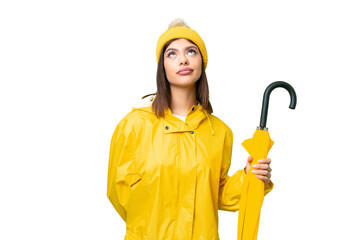 Young Russian woman with rainproof coat and umbrella over isolated chroma key background and looking up